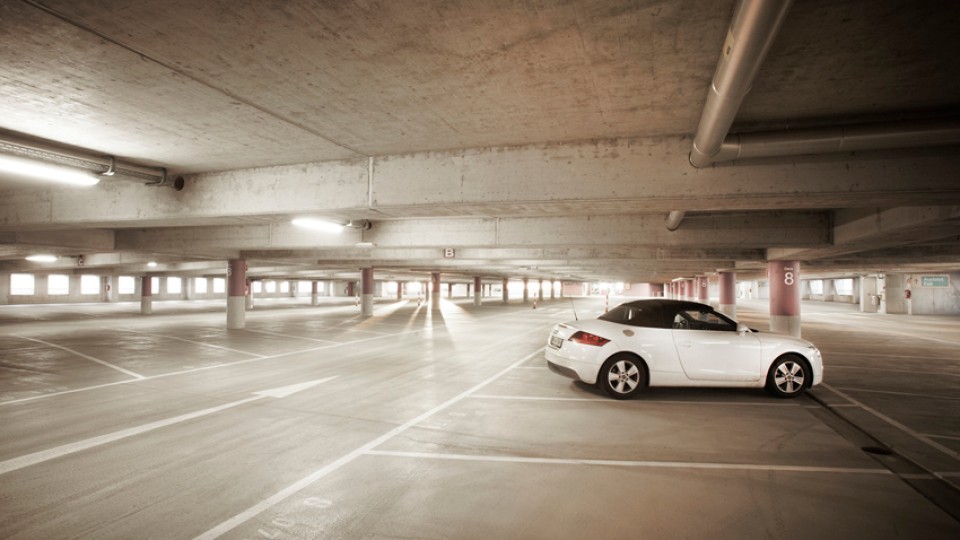 Ein fast leeres Parkhaus mit einem einzelnen weißen Cabrio, das in einer der markierten Parkbuchten steht. Die Szenerie ist hell ausgeleuchtet und wirkt sauber und geordnet.